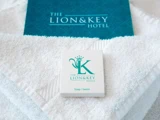 Et hvidt stykke sæbe og en blå brochure, begge med påskriften The Lion & Key Hotel, er placeret på sirligt foldede hvide håndklæder.