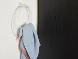 Et blåt håndklæde med en orange kant hænger på en hvid, rund håndklædering, der er monteret på en hvid væg ved siden af en mørk dør eller et mørkt panel.