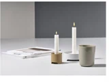 To hvide stearinlys i moderne stager, et beige krus og stablede magasiner på en hvid flade med grå baggrund.