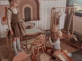 To små børn leger i et hyggeligt legerum i neutrale farver med rattanmøbler, dyrelegetøj og et vægtæppe med buer og en giraf.