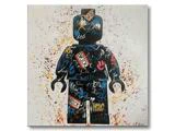 En farverig figur i LEGO-stil er dækket af graffiti og tags og står på en hvid baggrund, der er oversprøjtet med forskellige farver maling.