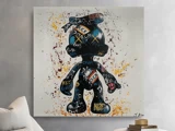 Et farverigt graffiti-maleri af en tegneseriefigur med ord og symboler over hele kroppen hænger på en lysegrå væg over en sofa.