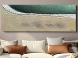 Et maleri med struktur, der forestiller havbølger ved en sandstrand, hænger over en hvid sofa med forskellige brune og beige puder.