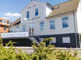 Hvid bygning med HOTEL MALLING og årstallene 1884 og 1914 på facaden, med en trappe, store vinduer og et terrassebanner med grønt i forgrunden.