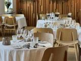 En moderne restaurant med træstole og borde dækket med hvide duge, glas, bestik og servietter, med en træpanelvæg i baggrunden.
