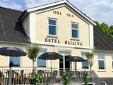 En lys bygning mærket Hotel Malling med årstallene 1884 og 1914, med en gårdhave med borde, stole og sorte parasoller foran.