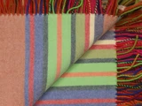 Nærbillede af et farverigt vævet tæppe med orange, grønne, blå, pink og røde striber og flerfarvede frynser langs kanterne.