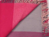 Et nærbillede af et frynset tæppe med et farveblokmønster i rosa og grå nuancer.
