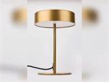En moderne bordlampe i guld med en rund fod, et slankt stativ og en bred, cylindrisk lampeskærm, fotograferet på en ensfarvet hvid baggrund.