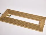 En rektangulær lamelramme af træ med en hul midte og et fastgjort cylindrisk metallisk lysarmatur på den ene side, placeret på en hvid baggrund.