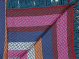 Et farverigt vævet tekstil med dristige striber i pink, rød, blå, orange og hvid, med et ombukket hjørne og frynsede kanter.