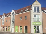 En murstensbygning med rødt tegltag og flere vinduer med en butiksfacade med grønne skilte med påskriften LOOP under en klar blå himmel.