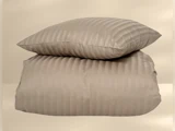 En beige, stribet pude hviler oven på en matchende stribet dyne på en neutral baggrund.