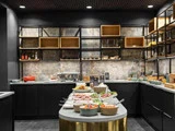 En moderne buffetopstilling i et slankt køkken med sorte skabe, åbne hylder og en række friske madretter arrangeret på en central ø.
