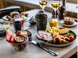 Et morgenbord med røræg, skinke, croissant, frugt, juice, kaffe og vin samt tallerkener og skåle med diverse madvarer i baggrunden.