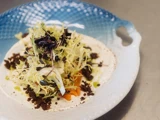 En gourmetsalat med frisésalat, mikrogrønt, grøntsager i tern, cremet sauce og knasende krummer på en hvid og blå keramiktallerken.