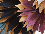 Nærbillede af lagdelte, spidse papirformer i sort, bordeaux og brun, arrangeret i et dekorativt mønster, der ligner overlappende blade eller kronblade.