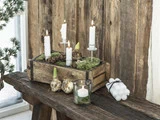 En rustik trækasse med hvide lys, mos, løg og kogler på en træbænk; ekstra lys og en glaslysestage står ved siden af.