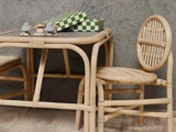 To flettede rattan-stole og et matchende bord med grøn- og hvidternede kasser og små legetøjssvampe på toppen, sat op mod en struktureret grå væg.