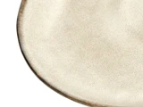 Et nærbillede af kanten på en rund, beige keramiktallerken med en let struktureret overflade og en tynd, mørk kant.