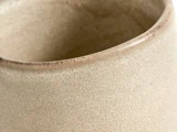 Nærbillede af kanten på en beige, struktureret keramisk kop eller gryde med en glat, let buet kant.