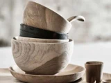 Stablede træskåle og en sort skål på en træplade med en lille kop ved siden af, alt sammen på en lys overflade.