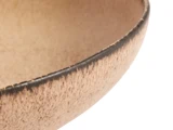 Nærbillede af en struktureret, beige keramikskål med mørk kant mod en hvid baggrund.