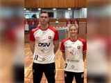 To håndboldspillere iført ens hvide og røde trøjer står på banen.