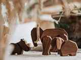 Tre dyrefigurer af træ, formet som et næsehorn, en elefant og en flodhest, står på et bord med en sløret naturbaggrund.
