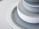 Et nærbillede af stablede, runde grå og hvide tallerkener og skåle, der er arrangeret pænt i faldende størrelse på en lys overflade.