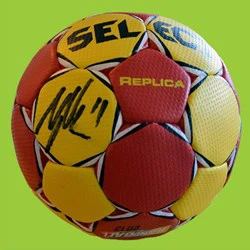 En rød og gul håndbold af mærket SELECT med en sort autograf, ordet REPLICA og en grøn baggrund.