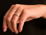 En hånd med en ring i guldtekstur på ringfingeren, fotograferet på en ensfarvet sort baggrund.