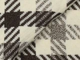 Nærbillede af et vævet stof med et geometrisk zigzagmønster i mørkebrune og cremefarvede nuancer, der viser tekstur og overlappende lag.