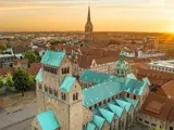 Luftfoto af Hildesheim i Tyskland ved solnedgang med historiske bygninger med grønne tage og et kirkespir i baggrunden.
