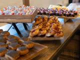 På et træbord står forskellige kager, desserter og små kopper med frugt eller salat, sirligt arrangeret på træbakker.