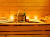 Et sauna-interiør i træ med spand, øse, håndklæder, olieflaske og stearinlys skaber en varm og afslappende atmosfære.