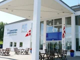 Indgangen til Løgstør Parkhotel med udendørsservering, to danske flag og glasdøre under en moderne hvid baldakin.