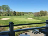 Udsigt fra en balkon over en golfbane med green, sandbunkers, træer og bænke på en solrig dag.
