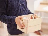 Et barn i en marineblå sweater holder en lys trækasse fyldt med pastelfarvet trælegetøj.
