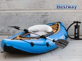 En blå oppustelig kajak med sort pagaj og luftpumpe er placeret på et gråt flisegulv ved siden af en betonvæg. Ordet Bestway står i øverste højre hjørne.