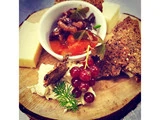 Et træfad med ostetern, knækbrød, ribs, friske krydderurter og en lille skål chutney eller relish.