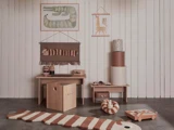 Minimalistisk børneværelse med træmøbler, indretning med dyretema, et lille skrivebord, opbevaringskasser og blødt legetøj i jordfarver mod en hvid panelvæg.
