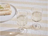 To glas hvidvin står på en stribet dug ved siden af en tallerken med hvide asparges.