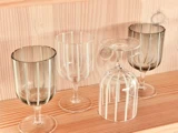 Fire gennemsigtige glas med lodrette striber står på en træhylde; det ene glas står på hovedet, mens de andre står oprejst.