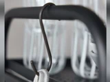 Et nærbillede af en mørk metal-S-krog, der hænger på en sort stang og holder fast i et hvidt klæde, med glasflasker, der fremstår slørede i baggrunden.
