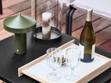 Et bord med en grøn lampe, et stearinlys i en glasholder, et bakke med en vinflaske, to tomme glas og en lille skål med oliven.
