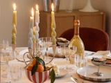 Et spisebord dækket med tændte stearinlys, vinglas, en flaske champagne, østers og en skål med mandariner på en hvid dug.