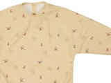 Langærmet, beige børnesmock med små brune dyre- og planteprint, med trykknaplukning bagpå tæt på kraven.