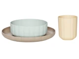 En beige tallerken, en lyseblå skål og en høj cremefarvet kop, alle med diskrete lodrette riller, præsenteret på en hvid baggrund.