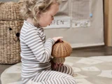 Et lille barn i stribet pyjamas sidder på et mønstret tæppe og holder en flettet kurv, der er formet som en svamp.